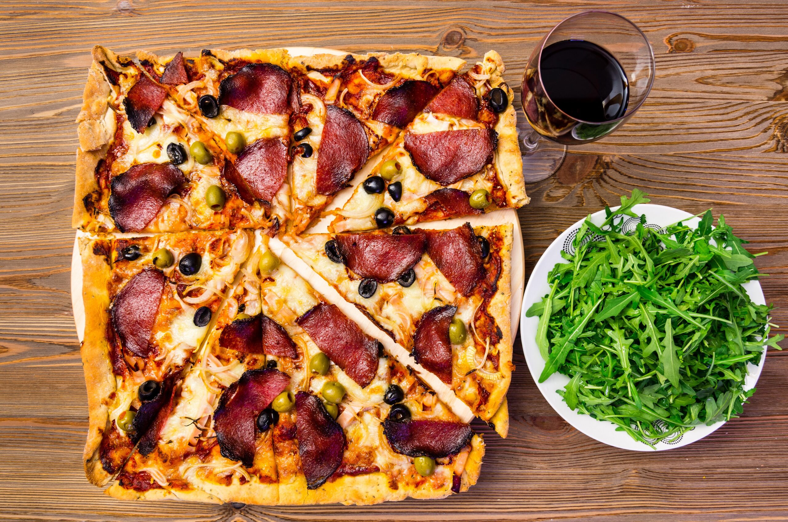 Pyszna domowa pizza lezy na stole koło rukoli i szklanki z napojem